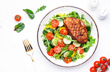 Fresh salad with grilled duck breast with red tomato, cucumber, paprika and chard, frisse, mizuna and arugula leaves on white table background, top view