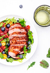 Duck slices salad with grilled breast and bloody orange, kumquat, blueberry and chard, frisse, mizuna, arugula leaves on white table background, top view