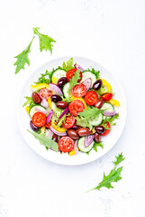 Vegan greek salad with kalamata olives, cherry tomato, yellow paprika, cucumber and red onion, healthy mediterranean diet food, low calories eating. White table background, top view