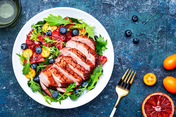 Duck salad with grilled breast with red orange, kumquat, blueberry and chard, frisse, mizuna and arugula leaves on blue table background, top view
