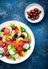 Vegan greek salad with kalamata olives, red tomato, yellow paprika, cucumber and onion, healthy mediterranean diet food, low calories eating. Blue stone background, top view