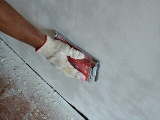 a worker's hand in a glove grinds a wall next to the floor strewn with fine dust from plaster using...