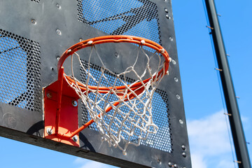 Public city park basketball hoop closeup with black industrial metal backboard and sunny blue sky
