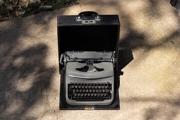 close-up gray typewriter with antique black cover on concrete floor giving sunlight and shade of tree with space for text