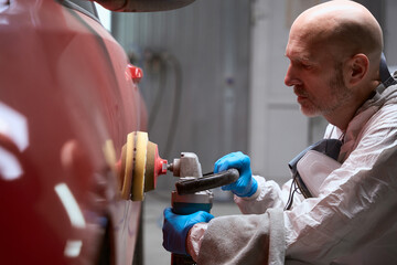Specialist in the repair shop polishes body of red car