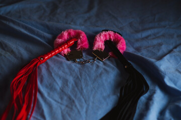 Handcuffs with red fur and a whip. Devices for love games on the bed.