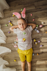 Bunny boy lying in room with easter eggs. Funny little Easter bunny child with easter egg. Easter kids portrait indoor. Top view funny kids laying on floor.