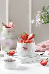 Chia pudding in a glasses with strawberries and oatmeal. White background, spring flowers.