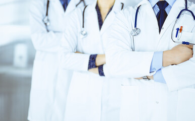 Group of modern doctors standing as a team with crossed arms and stethoscopes in hospital office. Physicians ready to examine and help patients.