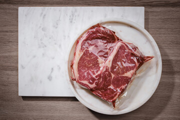 Vacuum packed meats. Raw beef steaks on white marble background, top view. Copy space.