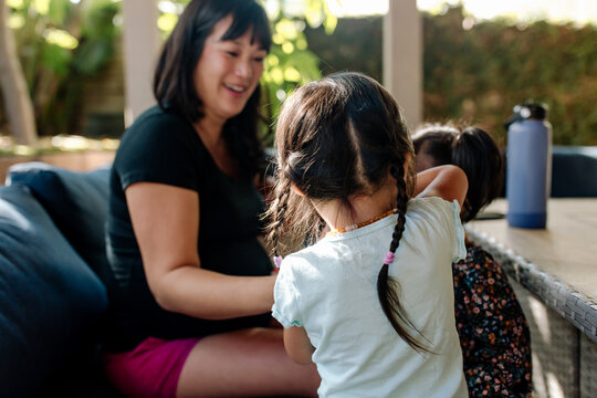 smiling pregnant mother outdoors on patio with her toddler daughters