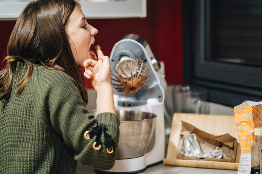 Girl trying chocolate batter in kitchen