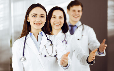 Fototapeta premium Doctors are standing as a team while offering their helping hands for shaking hand or saving people's life. Physicians are ready to help their patients. Medical help