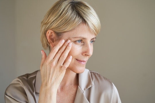 Middle aged woman applying cream on eye wrinkles