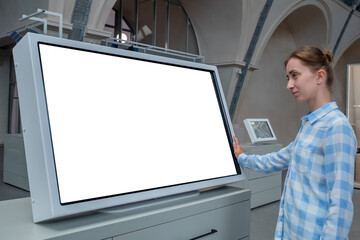 Woman in blue plaid shirt looking at blank interactive touchscreen white display of electronic kiosk at futuristic exhibition or museum. White screen, mock up, copyspace, template, technology concept.