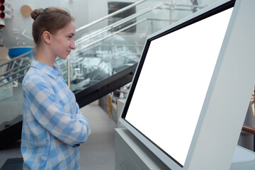 Side view: woman in blue plaid shirt looking at blank interactive horizontal white display of...