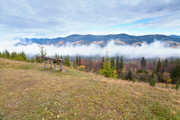 Wooden bench on top of mountain, view on the mountain ranges and fog. Ukraine, Carpathians.