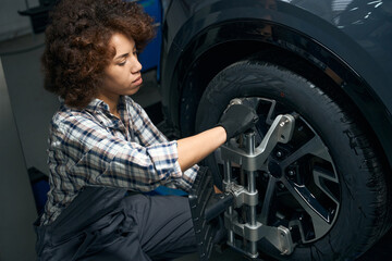 Fototapeta na wymiar Woman auto mechanic performs wheel balancing, adjusts wheel alignment