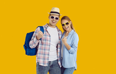 Joyful young Caucasian couple man and woman in sunglasses overjoyed about upcoming vacation trip on summer vacation getting ready for joint travel during honeymoon or holidays stands in yellow studio