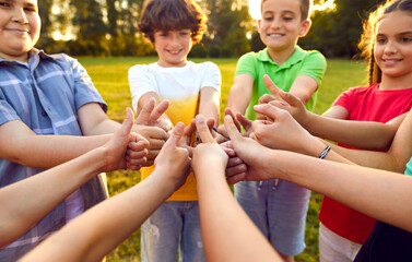 Happy children joining hands and giving thumbs up together. Croup of boys and girls standing in...