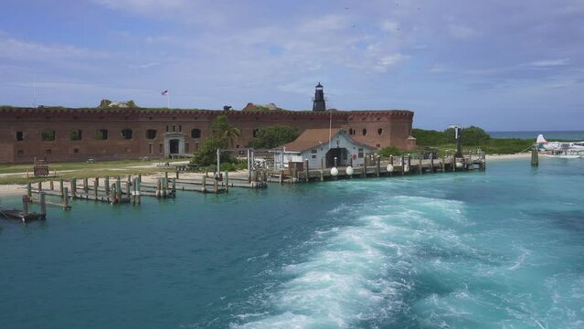 Fort Jefferson Boat Dock and house at Dry Tortugas National Park. A boat's wake, boat dock, brick fort, Garden Key Harbor Light lighthouse. Largest masonry fort in the Florida Keys was unfinished.
