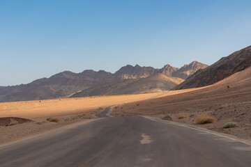 Panoramic view of endless empty road leading to colorful geology of multi hued Artist Palette rock formations in Death Valley National Park near Furnace Creek, California, USA. Black mountains