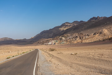 Panoramic view of endless empty road leading to colorful geology of multi hued Artist Palette rock formations in Death Valley National Park near Furnace Creek, California, USA. Black mountains