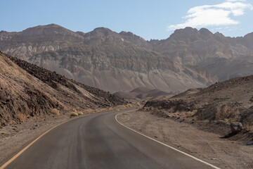 Panoramic view of endless empty road leading to colorful geology of multi hued Artist Palette rock formations in Death Valley National Park near Furnace Creek, California, USA. Black mountains