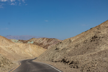 Panoramic view of endless empty road leading to colorful geology of multi hued Artist Palette rock formations in Death Valley National Park near Furnace Creek, California, USA. Black mountains