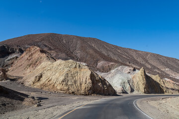 Panoramic view of endless empty road leading to colorful geology of multi hued Artist Palette rock formations in Death Valley National Park near Furnace Creek, California, USA. Black mountains