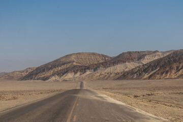 Panoramic view of endless empty road leading to colorful geology of multi hued Artist Palette rock formations in Death Valley National Park near Furnace Creek, California, USA. Black mountains