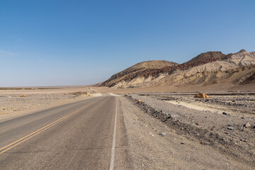 Panoramic view of endless empty road leading to colorful geology of multi hued Artist Palette rock formations in Death Valley National Park near Furnace Creek, California, USA. Black mountains