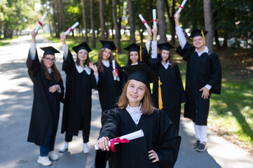 Happy young caucasian woman celebrating graduation with classmates. A group of graduate students outdoors.