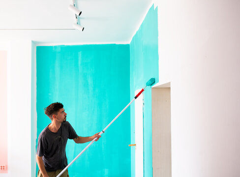 Graffiti artist preparing wall for mural with turquoise paint