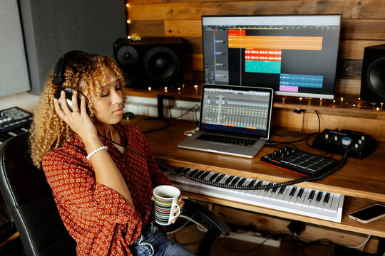 Audio producer at home studio listens to music track and drinks coffee