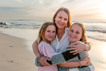 Fototapeta premium Portrait of mother holding her tween and teen daughters in her arms