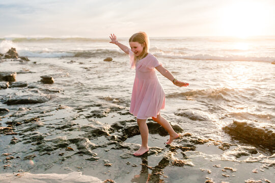 Happy tween girl in pink dress dancing on beach