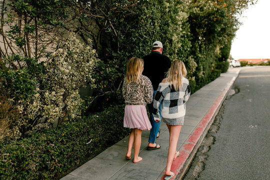 Father walking on side walk with his daughters