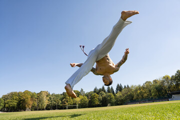 Athletic man in white pants, rising one leg jumping during workout