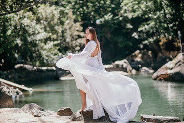 a beautiful woman in a long white dress looks into the distance at a beautiful lake with swans rear view