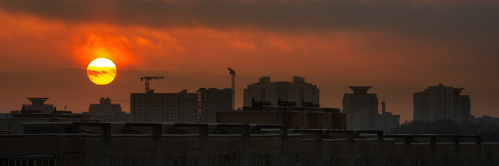 a dramatic red sunset over a city block with a sun disk above the rooftops. widescreen side view