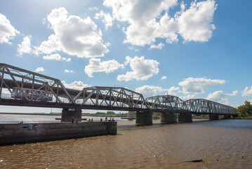 February, 12, 2016, Santa Lucía, Canelones, Uruguay: A bridge with a metallic structure that crosses a river, with a sky with clouds, while some people fish in a pier below the {el