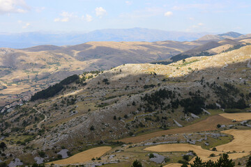 Fototapeta premium View of a mountain landscape with meadow, trees, steppe and buildings in Abruzzo in summer in Italy