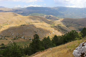View of a mountain landscape with meadow, trees, steppe and buildings in Abruzzo in summer in Italy
