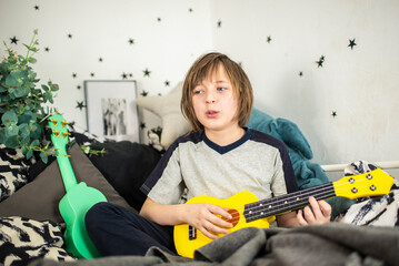 a little boy learns to play the yellow ukulele, a happy child sits in his bed, on black and white...