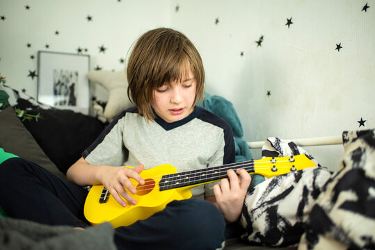 a little boy learns to play the yellow ukulele, a happy child sits in his bed, on black and white bed linen, plays the mini guitar and sings