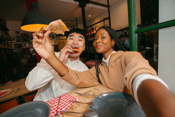 Selfie of Friends sharing pizza in restaurant having fun. UGC