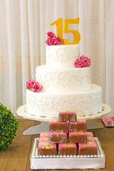 Bolo de aniversário de quinze anos e mesa decorada com flores e plantas.
