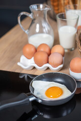 Various breads in baskets, 2 glasses and a mug with milk, oranges in a black dish and some eggs on the wooden table.