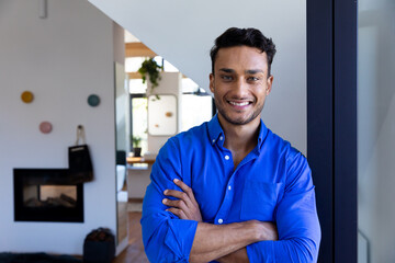Portrait of happy biracial man leaning on window and looking at camera